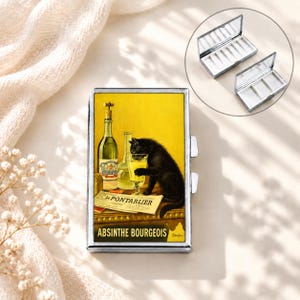 May include: A rectangular metal pill case featuring a vintage-style illustration of a black cat drinking from a glass next to an absinthe bottle and a newspaper titled Le Pontarlier. The bottom text reads Absinthe Bourgeois in black letters.