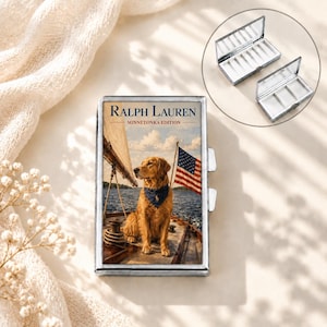 May include: A rectangular silver metal pill case featuring a printed image of a golden retriever wearing a blue bandana on a sailboat with an American flag. The text RALPH LAUREN MINNETONKA EDITION is printed above the dog. The case opens to reveal white compartments.