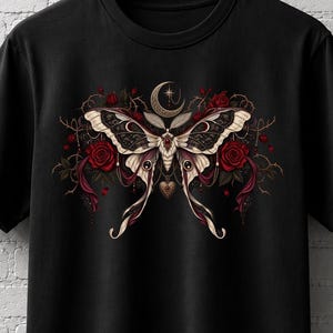 Può includere: Una t-shirt nera a maniche corte con una grafica centrale raffigurante una grande falena con intricati motivi sulle ali, circondata da rose rosso scuro, viticci spinosi scuri e un simbolo di luna crescente sopra la testa.