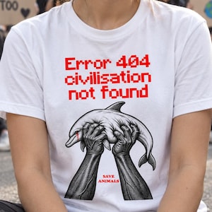 Może przedstawiać: Biały t-shirt z krótkim rękawem z nadrukiem graficznym zawierającym czerwony napis Error 404 civilisation not found nad czarno-białą ilustracją dwóch dłoni trzymających delfina, z czerwonym napisem SAVE ANIMALS umieszczonym pod dłońmi.