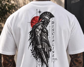 Könnte beinhalten: Ein weißes T-Shirt mit einer detaillierten schwarz-weißen Illustration eines spartanischen Kriegers mit Helm und Umhang, der ein Schwert hält. Hinter dem Krieger befindet sich eine rote kreisförmige Grafik mit dem vertikal gedruckten Text "DISCIPLINE" und "Earned, not given".