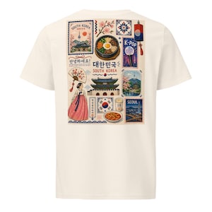Puede incluir: Una camiseta color crema con un estampado de collage en la espalda. El gráfico incluye ilustraciones de una persona con hanbok, un bol de bibimbap, un palacio tradicional, un abanico, una linterna, un lightstick y el texto South Korea y Seoul.