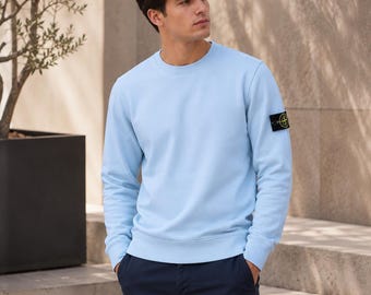 Può includere: Una felpa a maniche lunghe girocollo color azzurro con colletto, polsini e orlo a coste. Sulla manica sinistra è applicata una toppa con logo a forma di bussola nei colori nero, giallo e verde. Il capo è abbinato a pantaloni blu scuro.