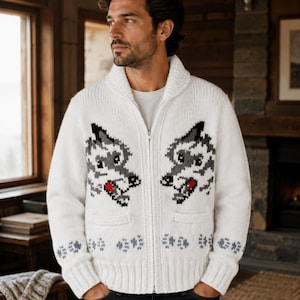 Pode incluir: Um cardig&atilde; de malha branca com fecho de correr, gola xale e um padr&atilde;o gr&aacute;fico de duas cabe&ccedil;as de lobo em cinzento, preto e vermelho. A camisola inclui dois bolsos frontais e um design repetitivo de pegadas cinzentas na bainha e nos punhos.