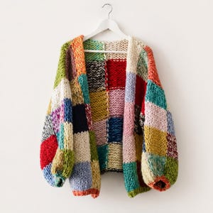 May include: A chunky knit cardigan featuring a patchwork design of large, multi-coloured squares. The garment is constructed from thick yarn in various shades including red, blue, yellow, green, pink, and cream, with long sleeves and an open front.
