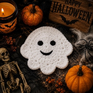 May include: A white crocheted ghost coaster with a smiling face featuring two round black eyes and a curved black mouth. The ghost has a scalloped edge and is crafted from yarn, displaying a textured, handmade appearance with a soft finish.