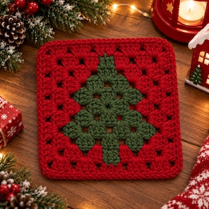 May include: A square crochet coaster featuring a red background with a dark green Christmas tree motif centered in the middle. The design is created using a classic granny square stitch pattern with visible yarn loops and a textured surface.