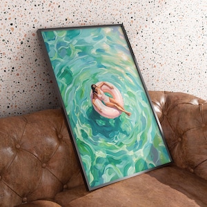 May include: A framed rectangular wall art print featuring an oil painting of a person in a white swimsuit floating on a pink circular inner tube in vibrant turquoise and green water with visible brushstrokes creating a rippling effect.