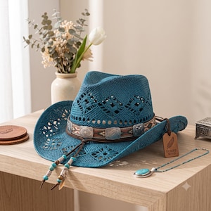May include: A teal straw cowboy hat featuring a woven diamond pattern, a brown leather band with silver-toned metal concho accents, and two dangling cords with turquoise beads. A brown leather tag attached to the hat reads Desert Wind.
