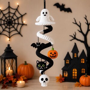 May include: A hanging crochet spiral decoration featuring a white ghost at the top, followed by a black bat, an orange jack-o'-lantern, a black cat head, and a white skull at the bottom. The spiral alternates between white and black yarn colors.