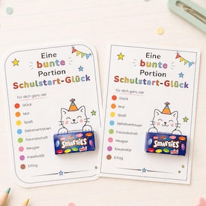 Puede incluir: Dos tarjetas rectangulares blancas tituladas Eine bunte Portion Schulstart-Glück, con un gato de dibujos animados con un sombrero de fiesta y una pequeña caja azul de caramelos Smarties mini. Las tarjetas enumeran palabras en alemán.