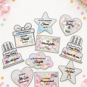 May include: A collection of nine clear plastic gift pouches in various shapes including stars, hearts, envelopes, and cakes. Each pouch contains colourful confetti and German text such as Happy Birthday, Sterne regnen, and Herzenswunsch.