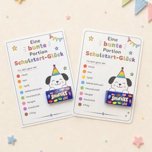 Puede incluir: Dos tarjetas rectangulares blancas con el texto Eine bunte Portion Schulstart-Glück, un perro de dibujos animados con un sombrero de fiesta arcoíris y una lista de palabras en alemán con puntos de colores. Una pequeña caja azul de Smarties Mini está pegada a cada tarjeta.