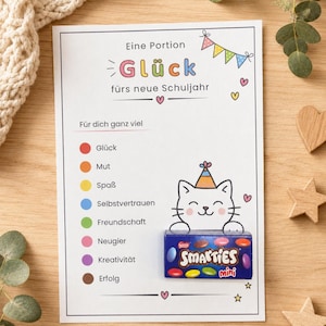 Könnte beinhalten: Eine weiße rechteckige Karte mit dem Text Eine Portion Glück fürs neue Schuljahr, einer Liste farbiger Kreise neben Wörtern wie Glück, Mut und Spaß sowie einer gezeichneten Katze mit Partyhut, die eine Schachtel Smarties mini in den Pfoten hält.