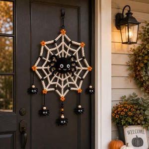 May include: A crocheted spider web wall hanging featuring a large central black spider with white eyes and a smiling mouth. The web is off-white with orange flower accents, black beads, and four smaller dangling black spiders at the bottom.