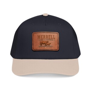 May include: A navy blue baseball cap with a beige brim and top button. Centered on the front is a rectangular brown leather patch featuring an embossed graphic of two cows and the text MERRELL LAND & LIVESTOCK DUNCAN, ARIZONA.