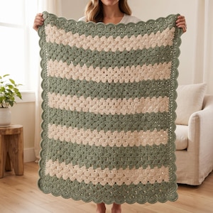 May include: A rectangular crochet blanket featuring alternating horizontal stripes of sage green and cream yarn. The blanket is constructed with a textured shell stitch pattern and is finished with a decorative scalloped border in sage green.