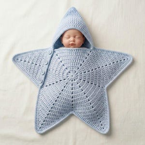 May include: A light blue crochet baby swaddle blanket shaped like a five-pointed star with a hood. The swaddle features a central circular pattern, radiating stitches, and a side closure with four small matching buttons to secure the garment.