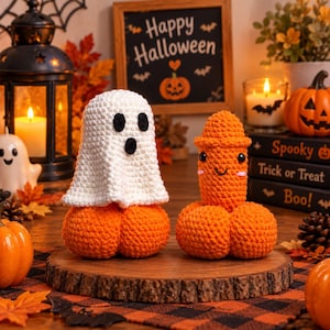 May include: Two crocheted amigurumi figures sitting on a wooden slice. One is a white ghost with black felt eyes and mouth perched on an orange pumpkin base. The other is an orange phallic-shaped figure with black eyes and a small smile.