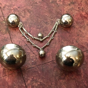 May include: A silver necklace with three round, silver charms. The necklace is made of two chains, and the charms are of different sizes.