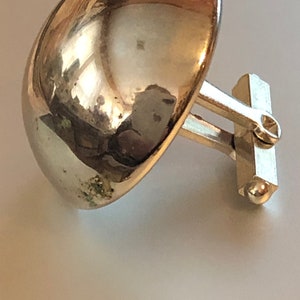 May include: A pair of silver cufflinks with a rounded, dome-shaped design. The cufflinks are attached to a silver bar with a small ball on the end.