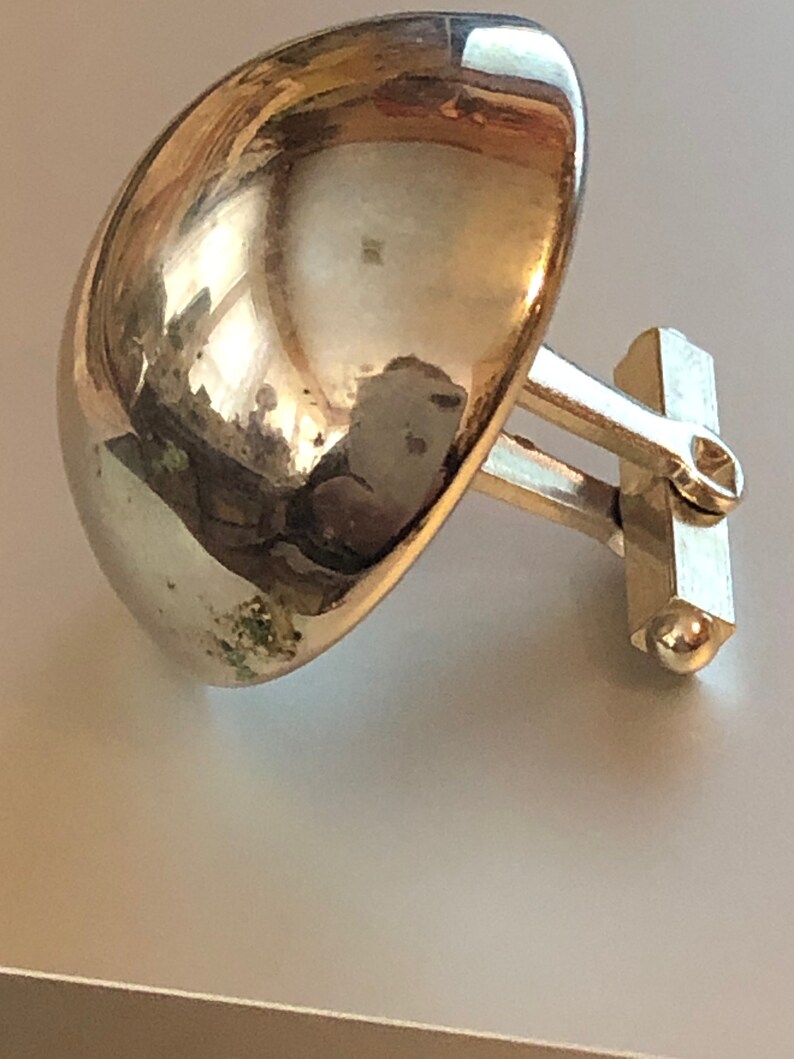 May include: A pair of silver cufflinks with a rounded, dome-shaped design. The cufflinks are attached to a silver bar with a small ball on the end.