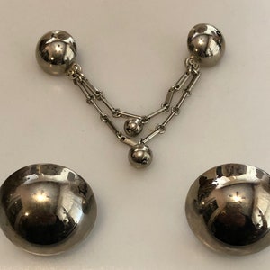 May include: A pair of silver-tone earrings with a dangling chain and three round balls. The earrings are made of metal and have a shiny finish.