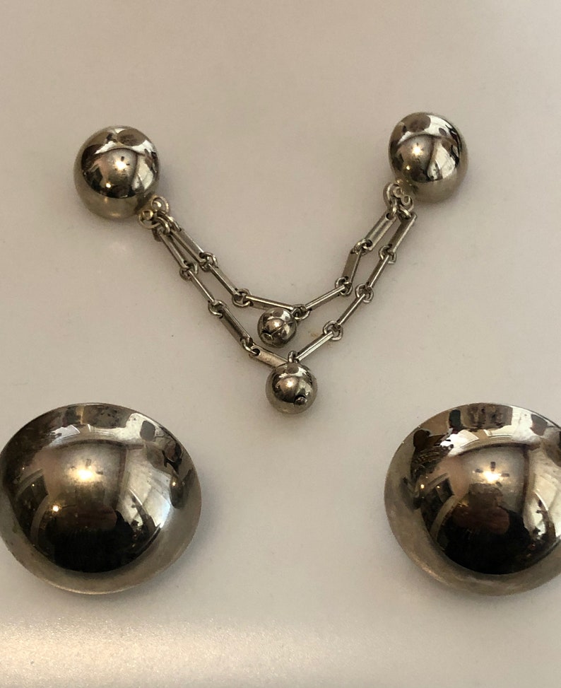 May include: A pair of silver-tone earrings with a dangling chain and three round balls. The earrings are made of metal and have a shiny finish.