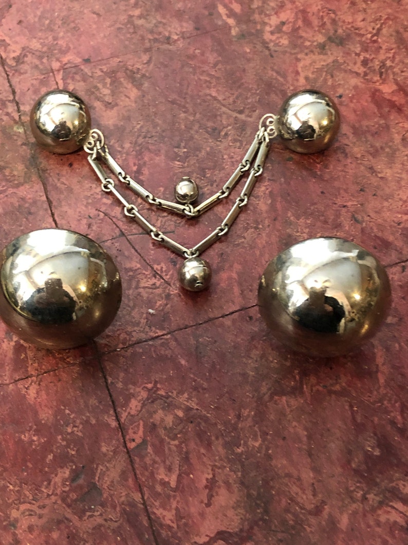 May include: A silver necklace with three round, silver charms. The necklace is made of two chains, and the charms are of different sizes.