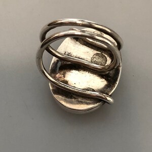 Pu&ograve; includere: Un anello d'argento con una grande pietra ovale incastonata al centro. La fascia dell'anello &egrave; attorcigliata e ha una finitura lucida.