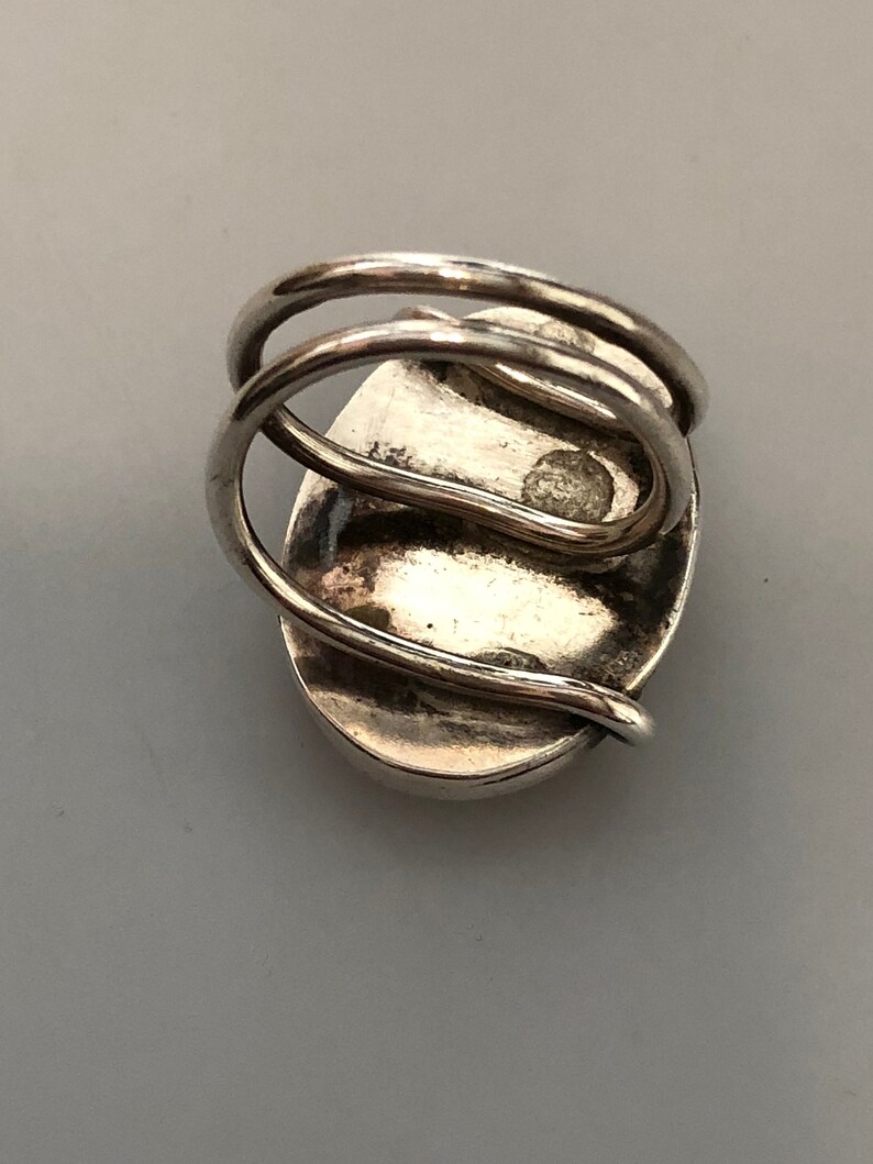 Pu&ograve; includere: Un anello d'argento con una grande pietra ovale incastonata al centro. La fascia dell'anello &egrave; attorcigliata e ha una finitura lucida.