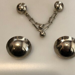 May include: A pair of silver tone clip-on earrings with a dangling chain and three round beads. The earrings are made of metal and have a shiny finish.