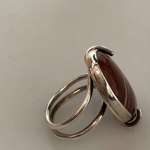 Pu&ograve; includere: Un anello d'argento con una pietra di agata rossa e bianca incastonata in una montatura a castone. L'anello ha una doppia fascia.