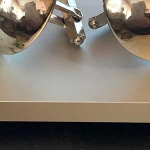 May include: A pair of silver cufflinks with a round, gold-toned design. The cufflinks are connected by a silver bar.