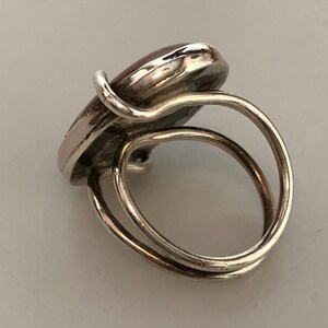 Pu&ograve; includere: Un anello d'argento con una pietra ovale rossa incastonata al centro. L'anello ha un design a doppia fascia.