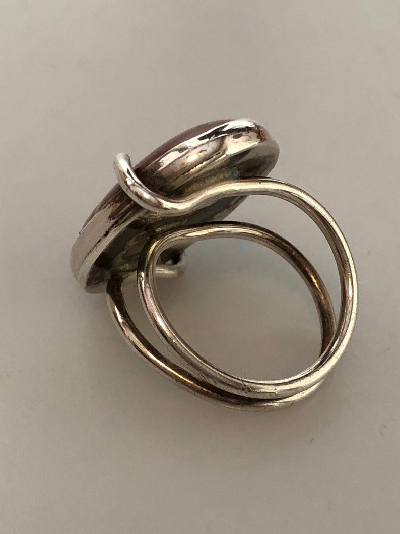 Pu&ograve; includere: Un anello d'argento con una pietra ovale rossa incastonata al centro. L'anello ha un design a doppia fascia.