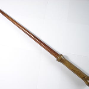 May include: A wooden wand with a brown and reddish-brown finish. The wand is approximately 33 cm long and has a rounded tip.