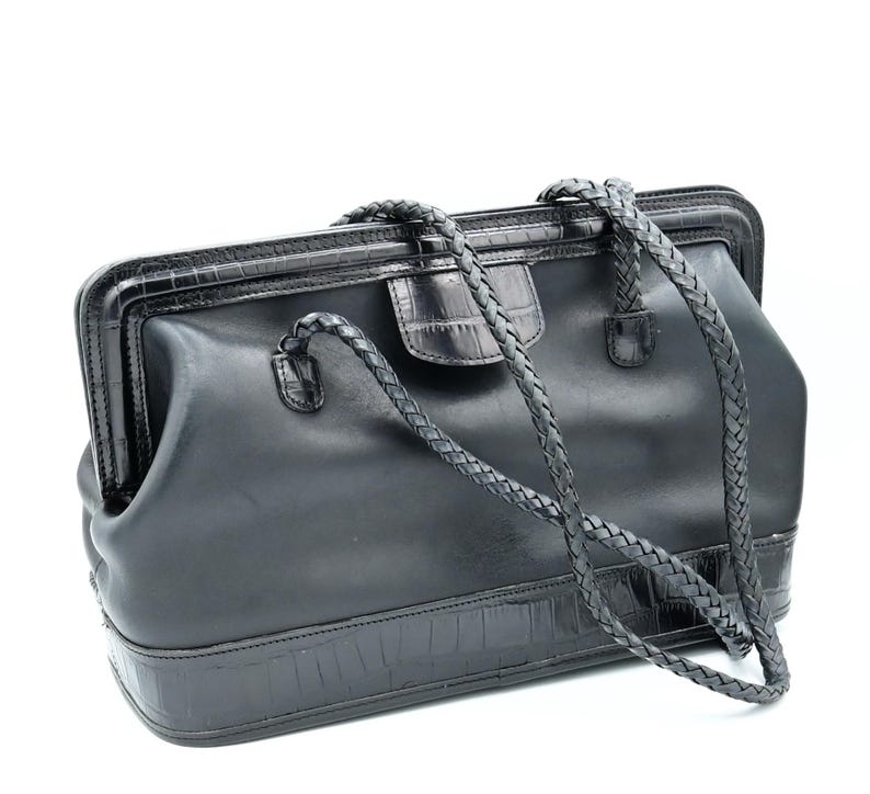 Puede incluir: Un bolso de m&eacute;dico de cuero negro con una correa trenzada y un patr&oacute;n de cocodrilo en relieve.