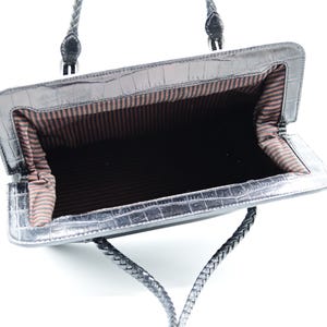 Puede incluir: Bolso de mano de cuero negro con asa trenzada y forro de rayas marrones. El bolso est&aacute; abierto y vac&iacute;o.