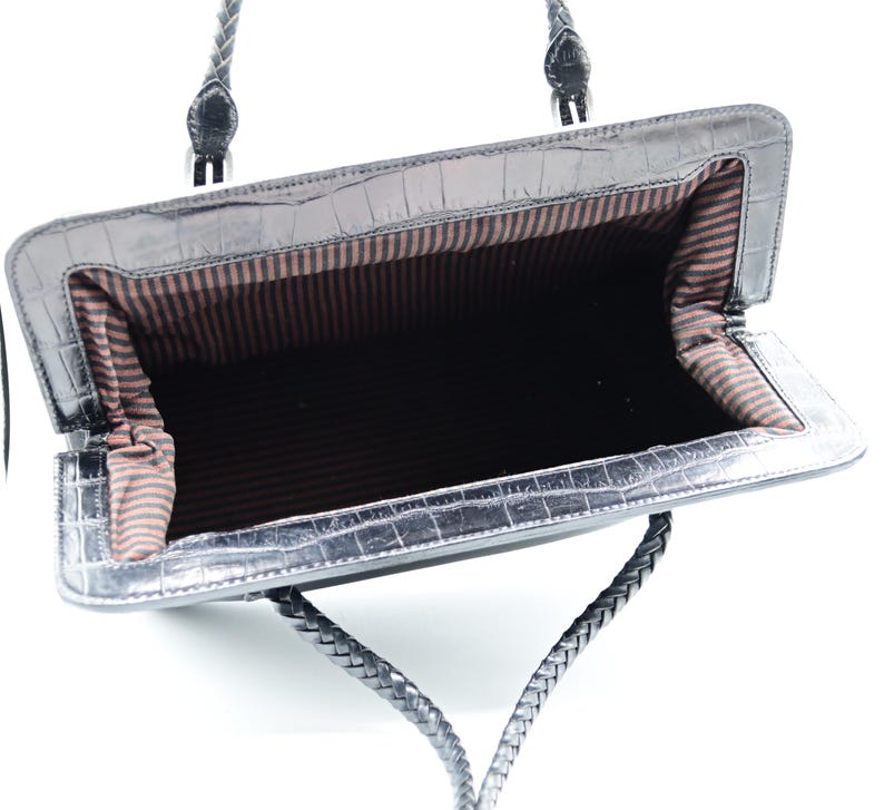 Puede incluir: Bolso de mano de cuero negro con asa trenzada y forro de rayas marrones. El bolso est&aacute; abierto y vac&iacute;o.