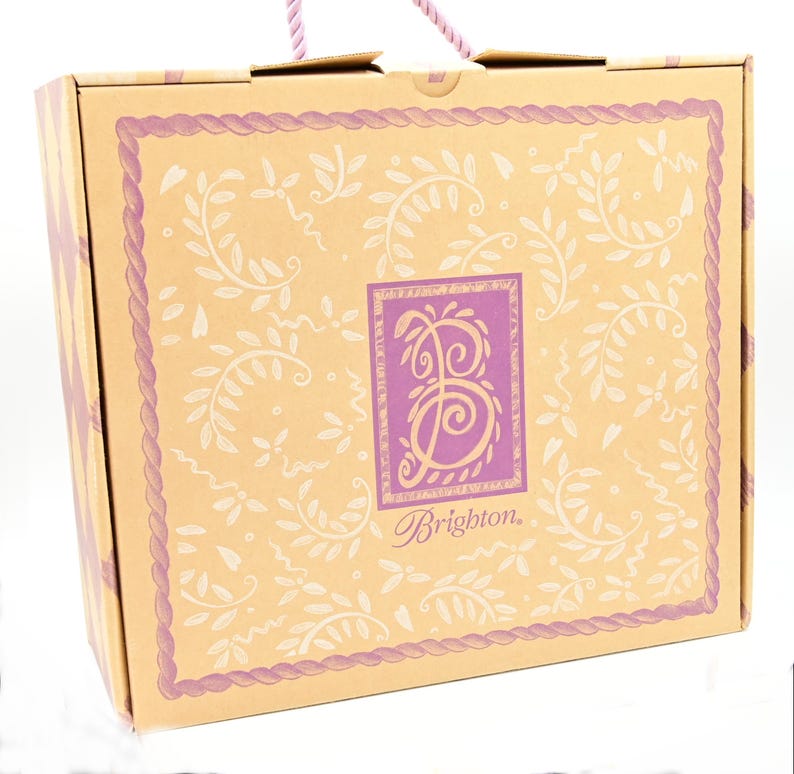 Puede incluir: Una caja de cart&oacute;n marr&oacute;n con un dise&ntilde;o floral morado y blanco. La caja tiene un asa y el texto "Brighton." impreso en la parte delantera.