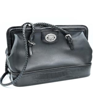 Puede incluir: Bolso de mano de cuero negro con una correa trenzada y una hebilla plateada. El bolso tiene una base con estampado de cocodrilo y un detalle decorativo plateado en la parte delantera.