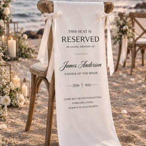 May include: A wooden chair draped with a white fabric memorial sign featuring black text that reads: THIS SEAT IS RESERVED IN LOVING MEMORY OF James Anderson FATHER OF THE BRIDE GONE BUT NEVER FORGOTTEN. FOREVER LOVED. ALWAYS IN OUR HEARTS.