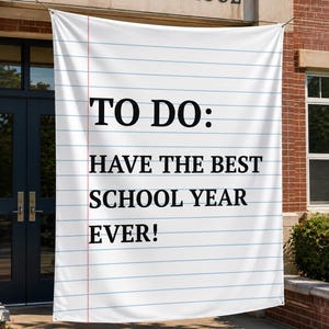 Peut inclure: Une grande bannière rectangulaire blanche conçue pour ressembler à une feuille de papier ligné avec une marge verticale rouge. Le texte en noir indique TO DO: HAVE THE BEST SCHOOL YEAR EVER! La bannière est suspendue devant un bâtiment en briques.