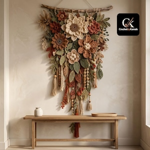 May include: A wall hanging featuring a collection of crocheted flowers and leaves in shades of cream, rust, and sage green, suspended from a wooden branch. The arrangement includes dangling tassels and wooden beads, with a logo reading CrochetbyKamals.