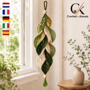 May include: A hanging crochet decoration featuring a vertical spiral of interconnected leaves in shades of dark green, light green, and cream. The piece is suspended by a crocheted loop with a wooden bead at the top and a green teardrop crystal at the base.