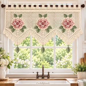 Puede incluir: Una cenefa de ganchillo color crema con tres flores rosas grandes y tridimensionales con hojas verde salvia. La cortina tiene una sección superior de rejilla, un borde inferior festoneado y tres detalles de hojas colgantes. El texto Crochetbykamals es visible.