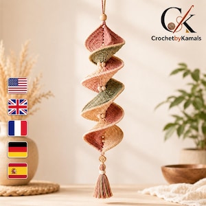 May include: A hanging spiral crochet ornament featuring alternating segments of dusty rose, sage green, and cream yarn. The structure is accented with small wooden beads between each section and terminates in a multi-colored yarn tassel at the bottom.