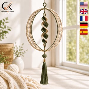 Pode incluir: Um ornamento de crochê suspenso com uma grande moldura circular com um padrão de treliça intrincado em bege e verde escuro. Um elemento central em espiral em bege e verde escuro alterna dentro do círculo, terminando em uma borla verde.