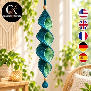 Può includere: Una decorazione a spirale sospesa realizzata in filato color verde acqua e verde chiaro. La struttura presenta un design ritorto continuo con una perla di legno nella parte superiore e inferiore. Il testo CrochetbyKamals è visibile in alto a sinistra.